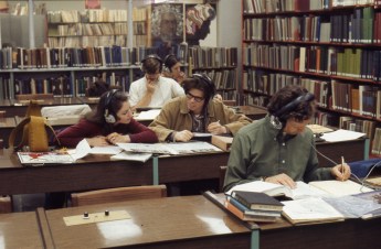 Students working at tables listen to headphones and look at books