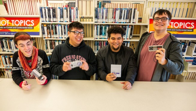 Four students pose in the Library with vintage video game equipment