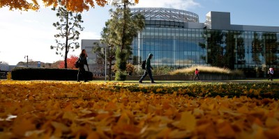 Students walking in front of the Fresno State Library with fall leaves on the ground