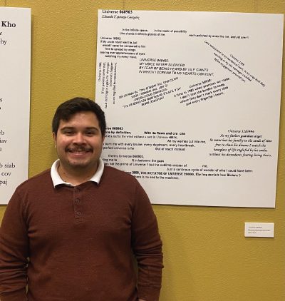 Eduardo Espinoza-Gonzalez stands next to his visual poem, a large posterboard with poetry verses arranged in a graphical layout
