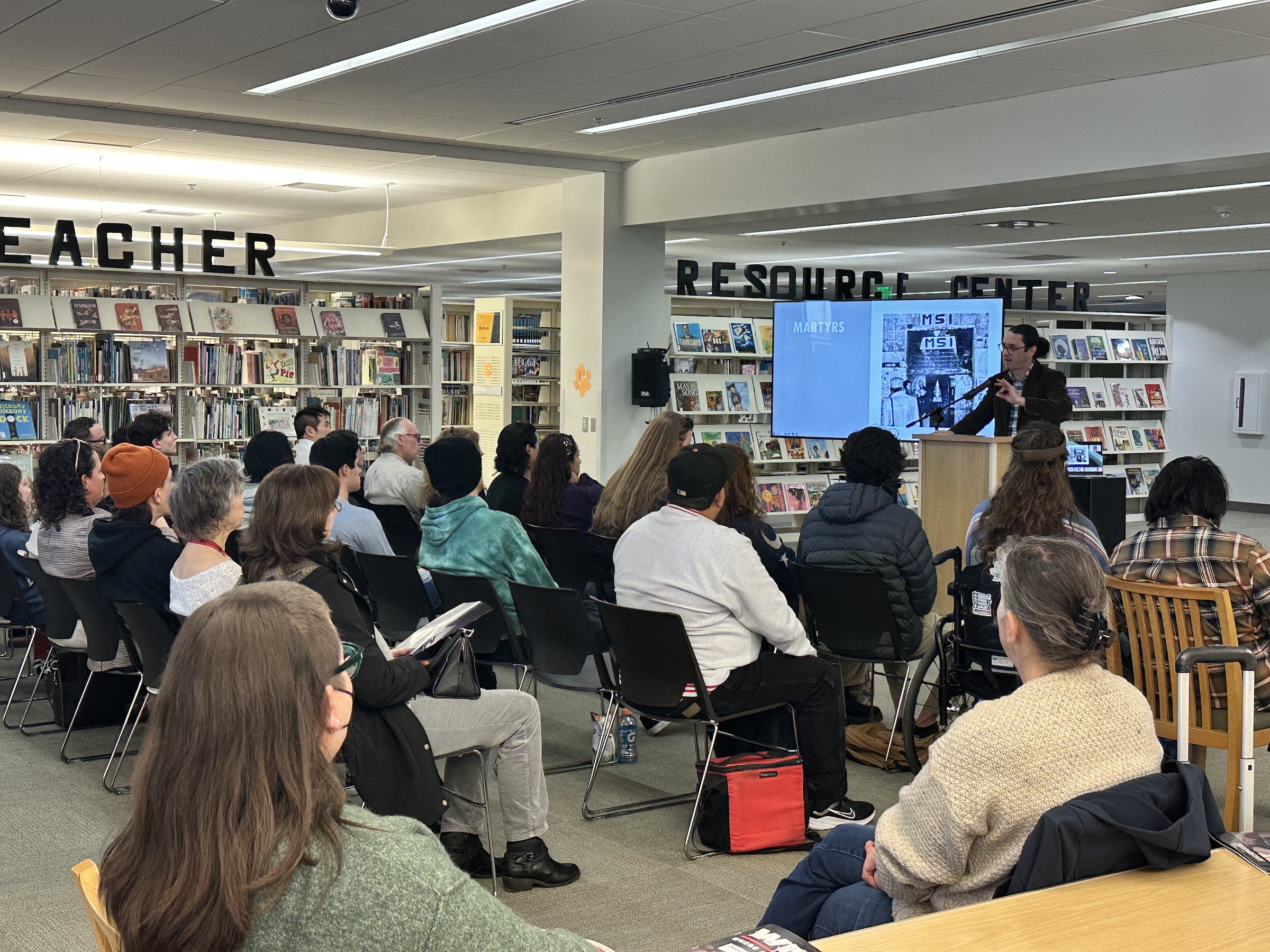 Dr. Griffith speaking at the podium with multimedia playing behind - large crowd seated in front