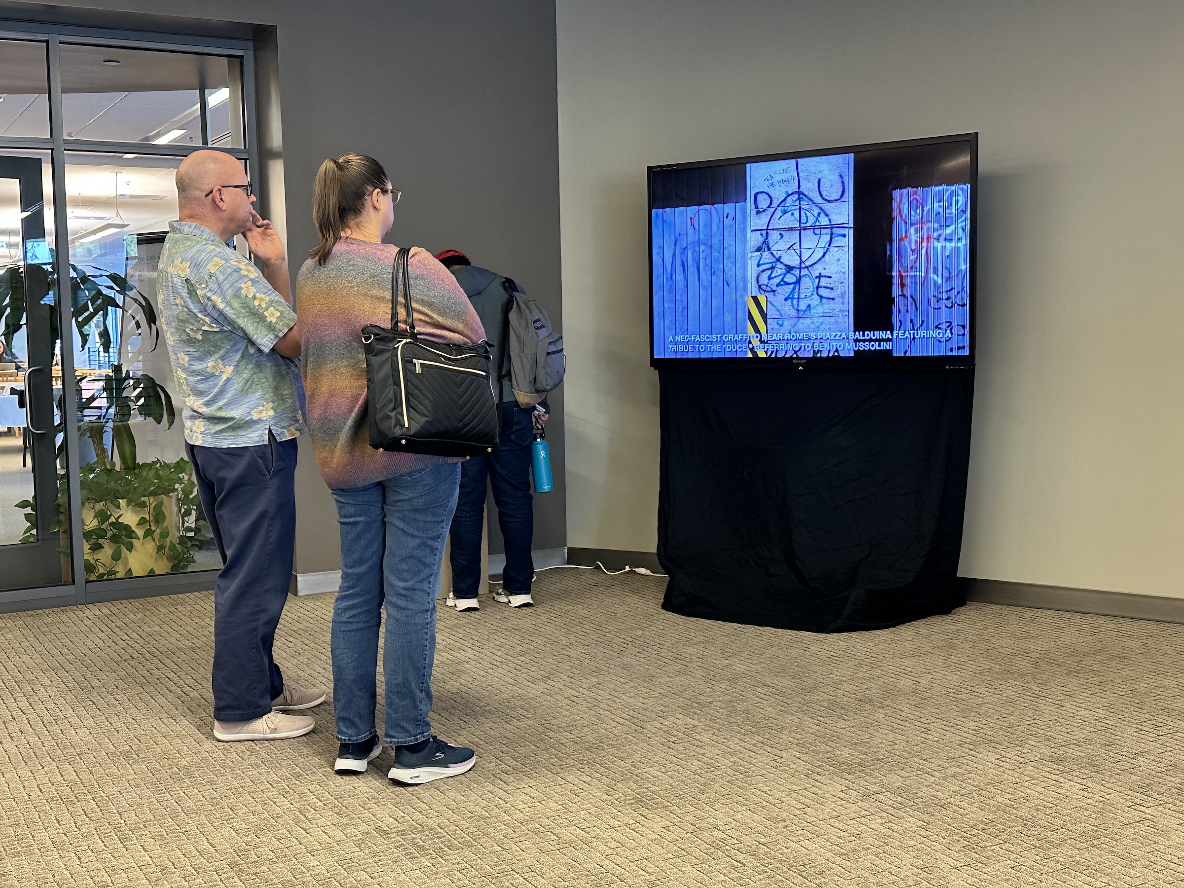 two attendees watch the multimedia portion of the exhibition