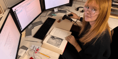 student intern sits at desk with three monitors and several books