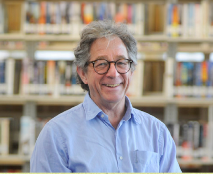 Jim Silverman smiles for a portrait in front of library shelves full of books. 